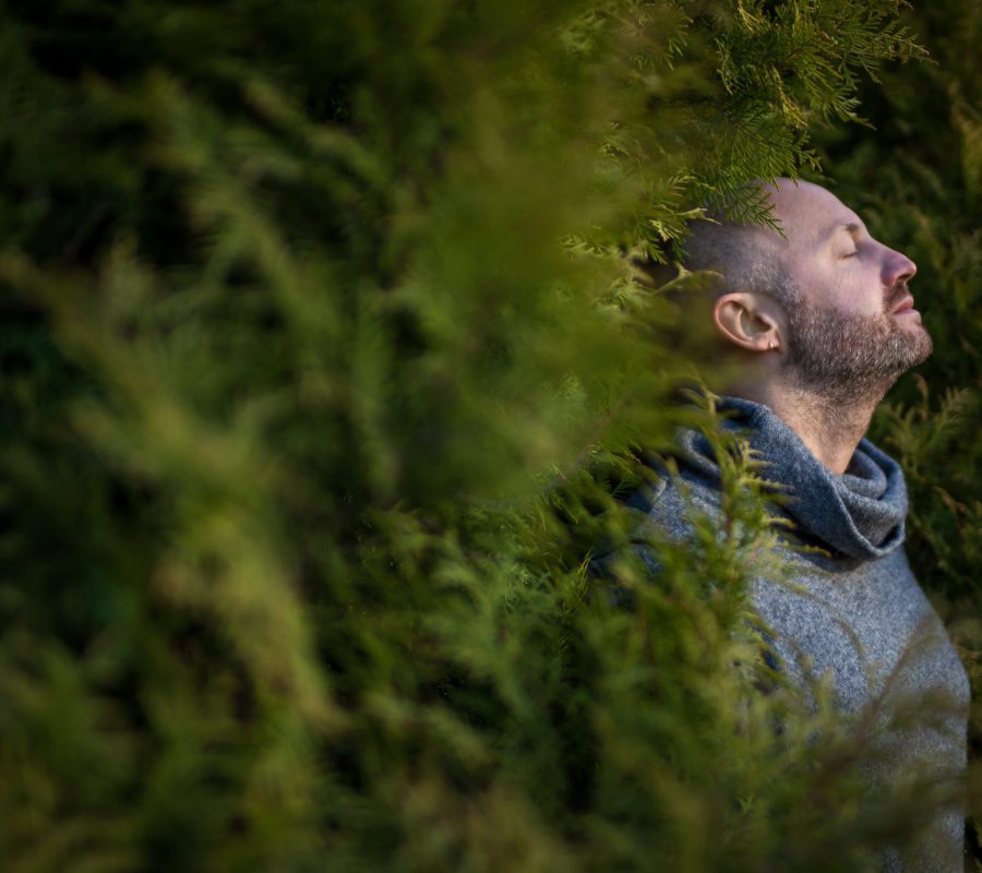 A bald man in a warm sweater is resting, leaning against the trees. Breathe fresh air in nature.